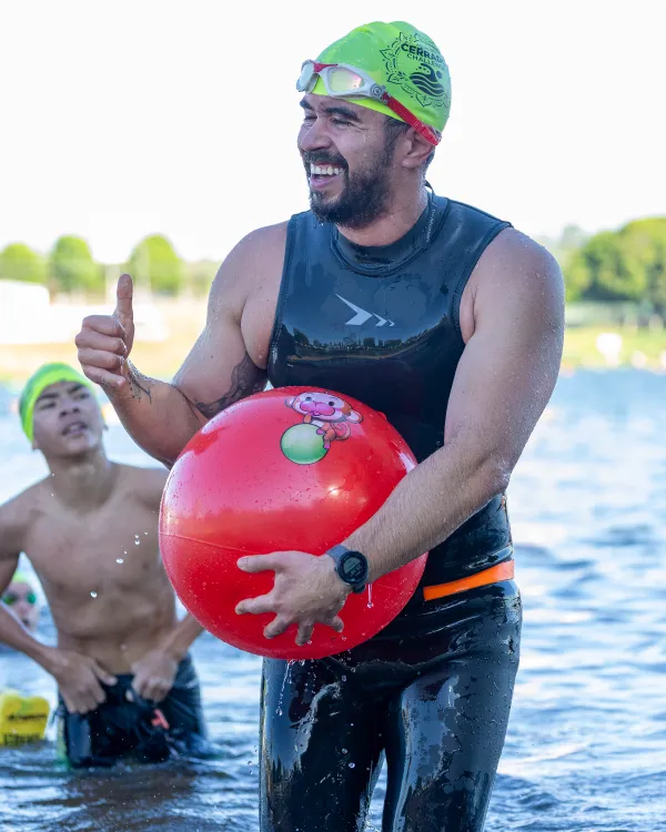 Nadador comemora ao sair da água segurando a boia de segurança vermelha